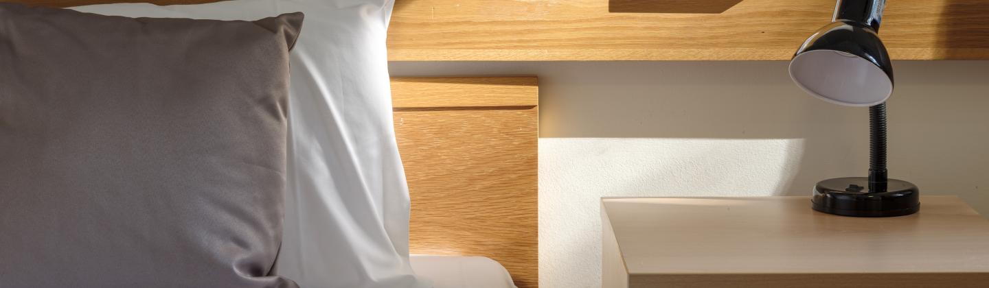 Close up image of a bed and side table with ray of light across pillow