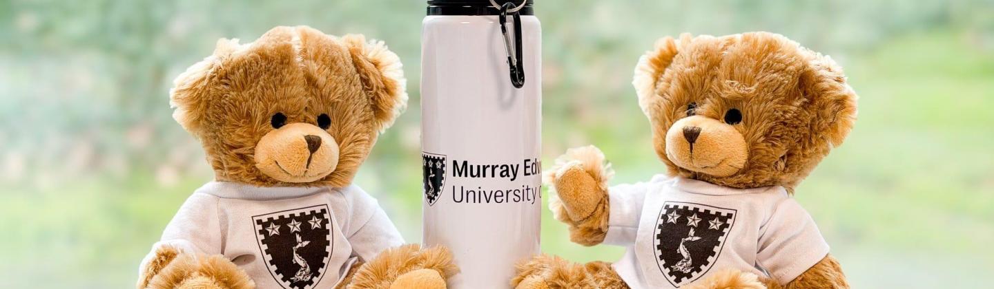 Two teddy bears wearing a t-shirt with the college crest. A white, similarly-branded water bottle in the centre.