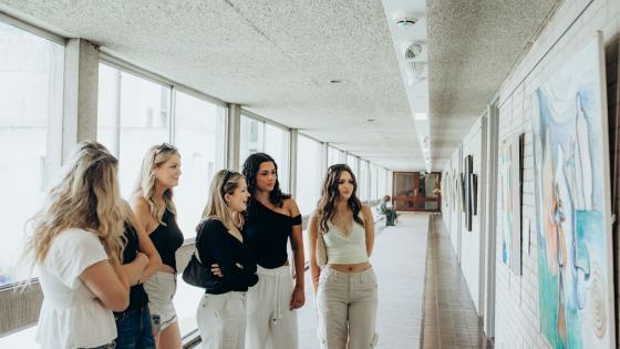 Five young women in a gallery corridor looking at an art work