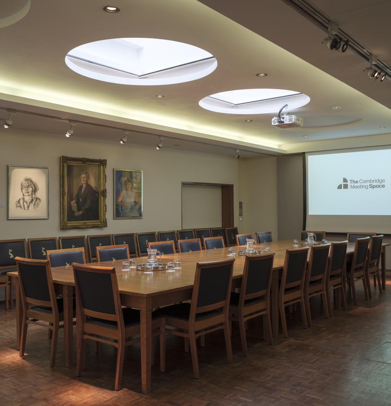 Meeting room with long table and chairs down either side. Projector and screen at the end with art work on the walls.